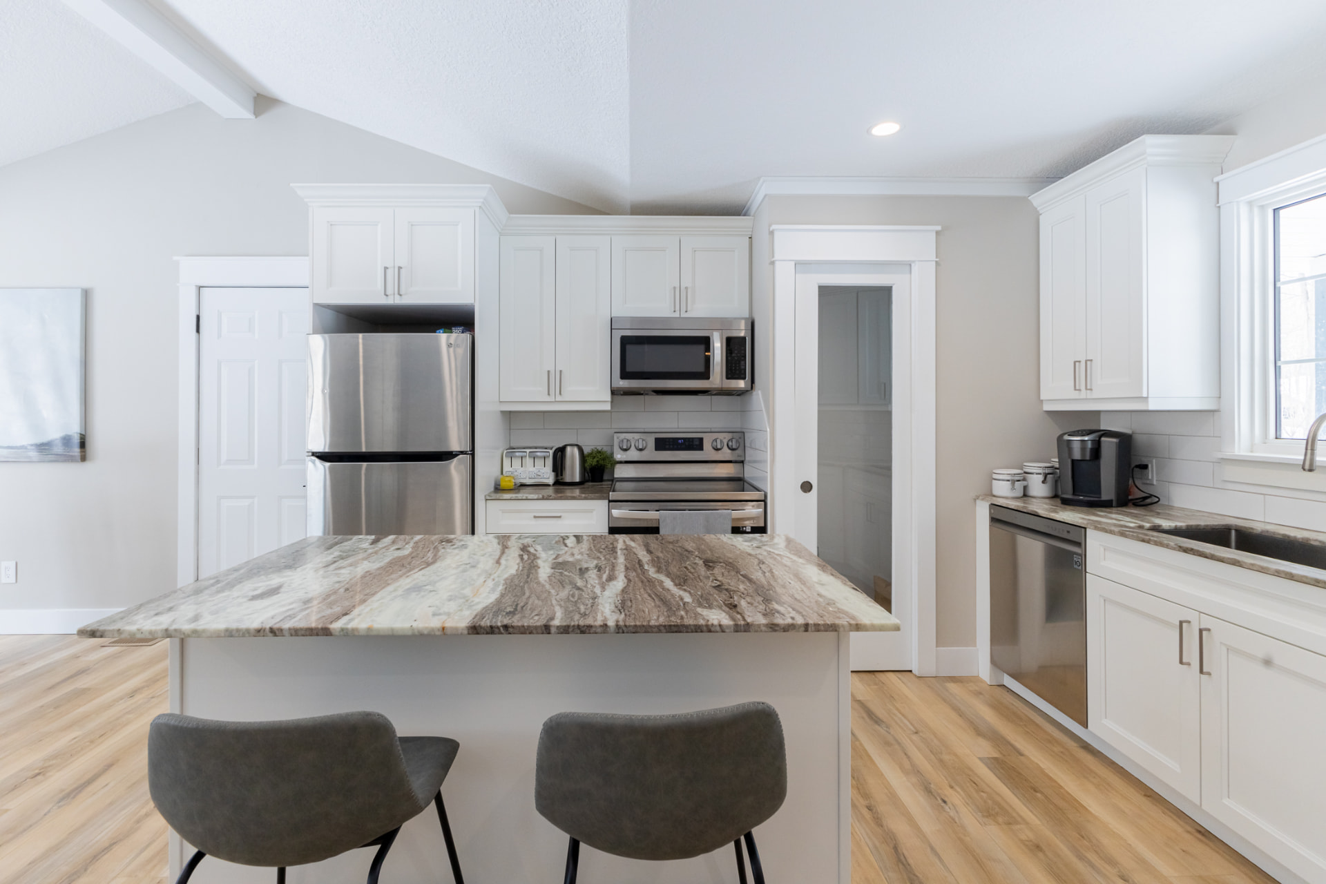 Finished kitchen island with bar seating framed by white cabinetry and vaulted ceiling